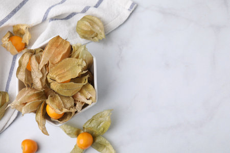 Ripe physalis fruits with calyxes in bowl on white marble table, flat lay. Space for textの写真素材