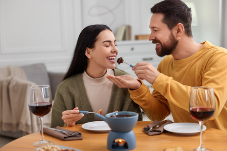 Affectionate couple enjoying chocolate fondue during romantic date at homeの写真素材