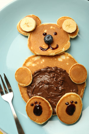 Creative serving for kids. Plate with cute bear made of pancakes, blueberries, bananas and chocolate paste, top viewの写真素材