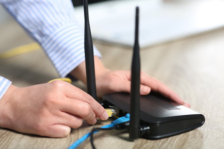 Woman inserting ethernet cable into Wi-Fi router at table indoors, closeupの写真素材