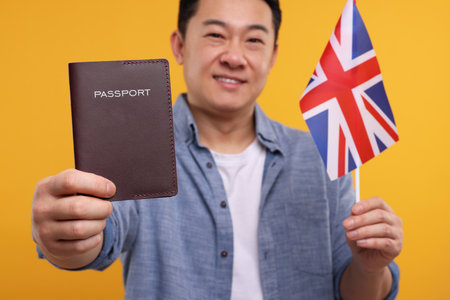 Immigration. Happy man with passport and flag of United Kingdom on orange background, selective focusの写真素材
