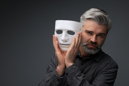 Multiple personality concept. Man with mask on dark gray background, space for textの写真素材