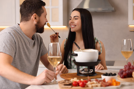 Affectionate couple enjoying cheese fondue during romantic date in kitchenの写真素材