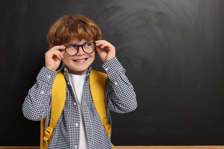 Happy schoolboy in glasses with backpack near blackboard, space for textの写真素材