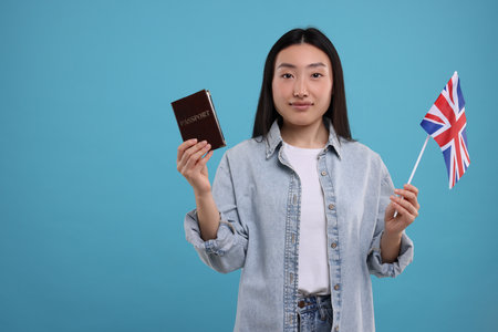 Immigration to the United Kingdom. Woman with passport and flag on light blue background, space for textの写真素材