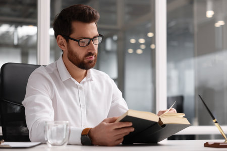 Handsome man reading book at table in office, space for text. Lawyer, businessman, accountant or managerの写真素材