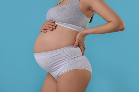 Pregnant woman in comfortable maternity underwear on light blue background, closeupの写真素材