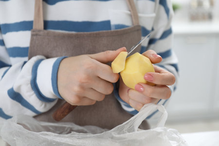 Woman peeling fresh potato with knife at white marble table indoors, closeupの写真素材