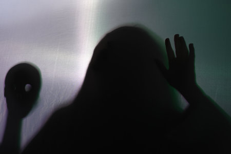 Silhouette of creepy ghost with skull behind cloth against gray backgroundの写真素材