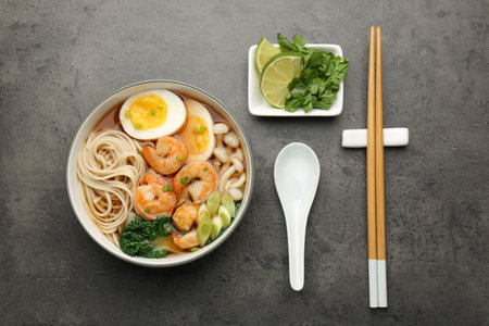 Delicious ramen with shrimps and egg in bowl served on gray table, flat lay. Noodle soup