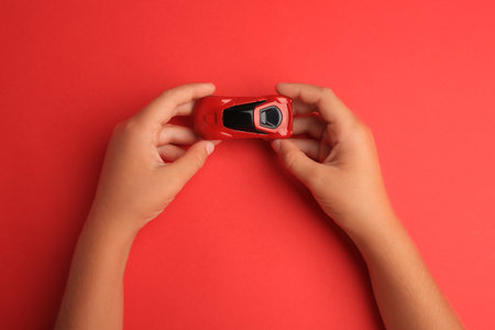 Child holding toy car on red background, top view