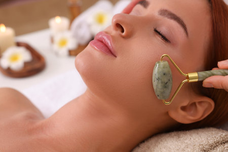 Young woman receiving facial massage with jade roller in beauty salon, closeupの写真素材