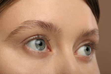 Woman with beautiful natural eyelashes on light brown background, closeupの写真素材