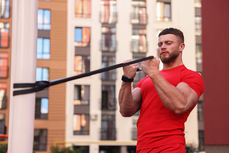 Muscular man doing exercise with elastic resistance band on sports ground