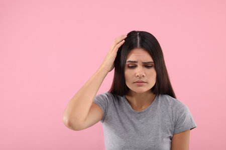 Emotional woman examining her hair and scalp on pink background, space for text. Dandruff problemの写真素材