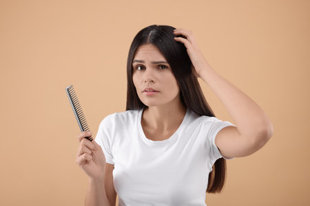 Emotional woman with comb examining her hair and scalp on beige background. Dandruff problemの写真素材