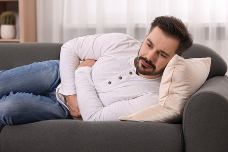 Man suffering from stomach pain on sofa at homeの写真素材