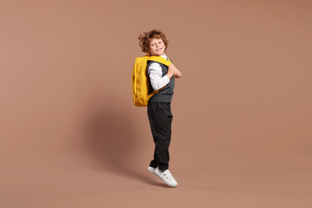 Happy schoolboy with backpack jumping on brown backgroundの写真素材
