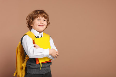 Happy schoolboy with backpack and books on brown background, space for textの写真素材