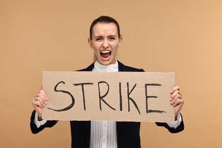 Screaming woman holding cardboard banner with word Strike on beige backgroundの写真素材