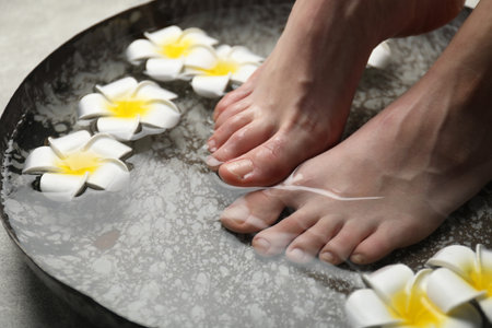Woman soaking her feet in bowl with water and flowers on floor, closeup. Spa treatmentの写真素材