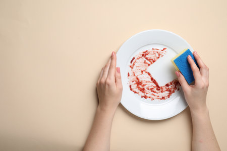 Woman washing dirty plate with sponge on beige background, top view. Space for textの写真素材