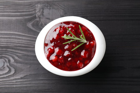 Fresh cranberry sauce in bowl and rosemary on black wooden table, top viewの写真素材
