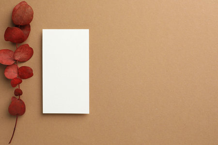 Blank business card and red eucalyptus branch on beige background, flat lay. Mockup for design