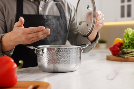 Man with pot smelling dish after cooking at white marble countertop in kitchen, closeupの写真素材