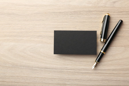 Blank black business card and fountain pen on wooden table, flat lay. Mockup for designの写真素材