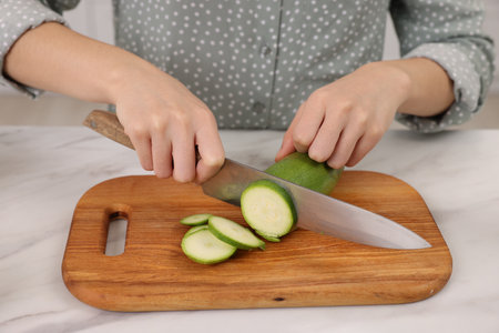 Cooking process. Woman cutting zucchini at white marble countertop, closeupの写真素材