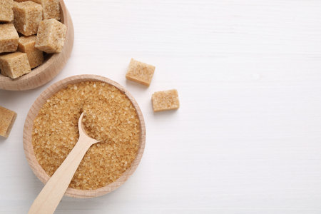 Bowls and spoon with different types of brown sugar on white wooden table, flat lay. Space for textの写真素材