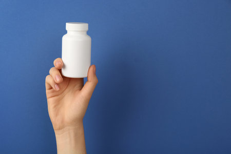 Woman holding blank white jar of vitamins on blue background, closeup. Space for textの写真素材