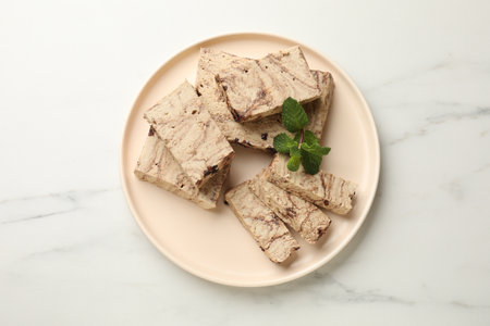 Pieces of tasty chocolate halva and mint on white marble table, top view
