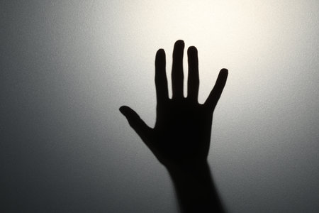 Silhouette of creepy ghost behind glass against gray background, closeup. Space for text