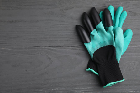 Pair of claw gardening gloves on gray wooden table, top view. Space for text