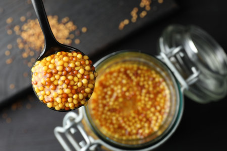 Spoon with whole grain mustard over jar on table, closeup