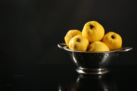 Tasty ripe quinces with water drops in metal colander on black background, space for textの写真素材