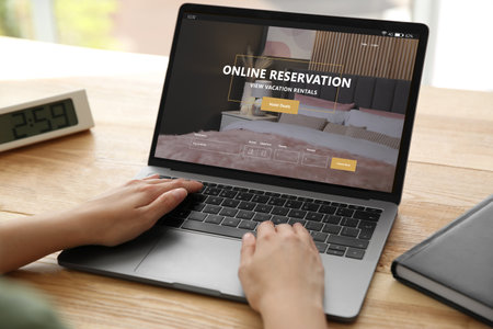 Woman using laptop to book hotel at wooden table, closeup