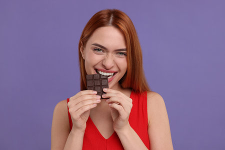Young woman eating tasty chocolate on purple backgroundの写真素材
