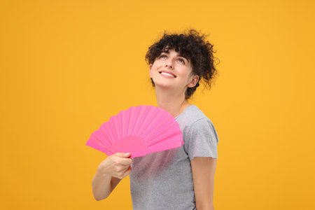 Happy woman holding hand fan on orange backgroundの写真素材