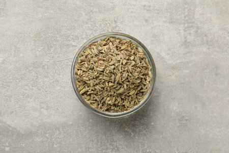 Fennel seeds in bowl on gray table, top view