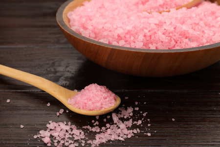 Bowl and spoon with pink sea salt on wooden table, closeup