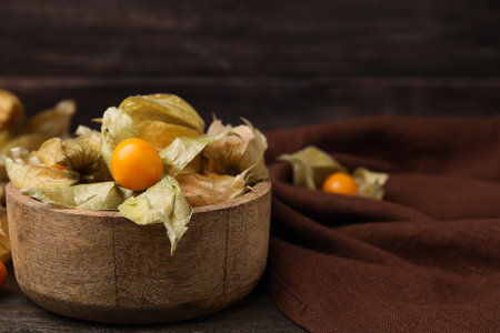 Ripe physalis fruits with calyxes in bowl on wooden table, space for textの写真素材