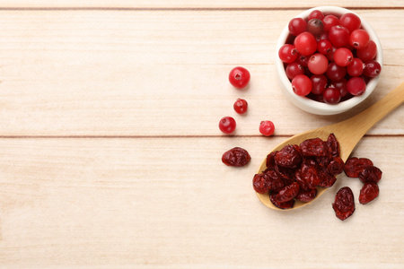 Spoon with dried cranberries and fresh berries in bowl on wooden table, flat lay. Space for text