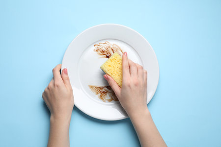 Woman washing dirty plate with sponge on light blue background, top viewの写真素材