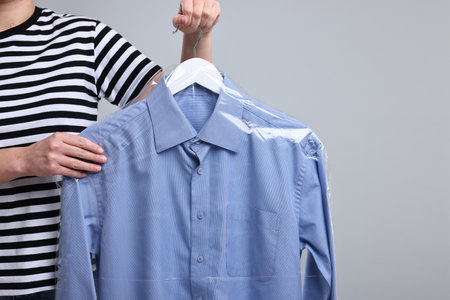 Dry-cleaning service. Woman holding shirt in plastic bag on gray background, closeup. Space for textの写真素材