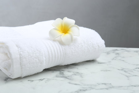 Folded terry towel and plumeria flower on white marble table, closeup. Space for textの写真素材