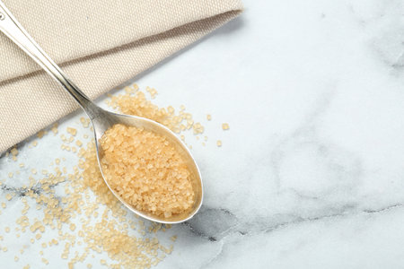 Spoon with brown sugar on white marble table, top view. Space for textの写真素材