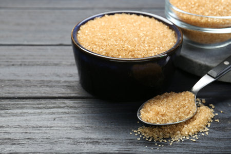 Brown sugar in bowls and spoon on black wooden table, closeup. Space for textの写真素材